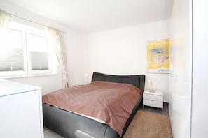 A bedroom with a bed, a bedside table, a lamp, a wardrobe, and a window with curtains.