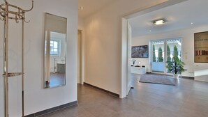 A modern interior with a large mirror, a hallway leading to a bathroom, a living area with a TV, and a bookshelf.