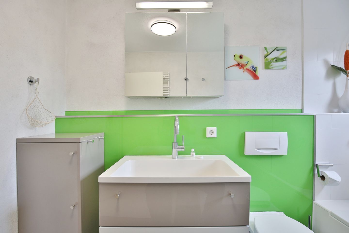 A bathroom with a white sink, green wall, and a cabinet.