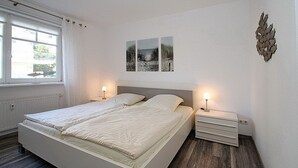 Une chambre à coucher avec un lit double, deux tables de chevet avec des lampes, un radiateur et une fenêtre avec des rideaux.