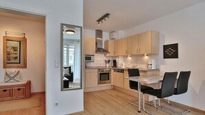 Une cuisine moderne avec des meubles en bois, un coin repas comprenant une table et des chaises, et un miroir qui reflète la pièce.