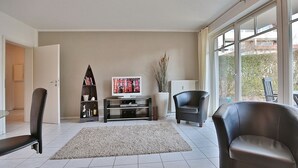 A living room with a TV, a bookshelf, two leather chairs, a large window, and a door leading to another room. - Strandstrasse 150 Apartment 02 - House Strandstrasse (Timmendorfer Strand)