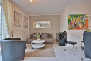 A modern living room with a sofa, a coffee table, a TV, and a painting on the wall. - Strandstrasse 150 Apartment 02 - House Strandstrasse (Timmendorfer Strand)