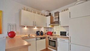 A modern kitchen with white cabinets, a red kettle, a microwave, an oven, and a sink. - Strandstrasse 150 Apartment 02 - House Strandstrasse (Timmendorfer Strand)