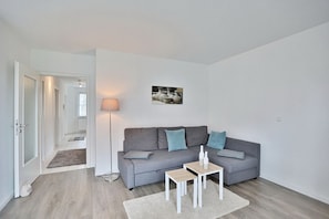 Un salon moderne avec un canapé gris, deux tables d’appoint, une lampe sur pied et un petit tapis.