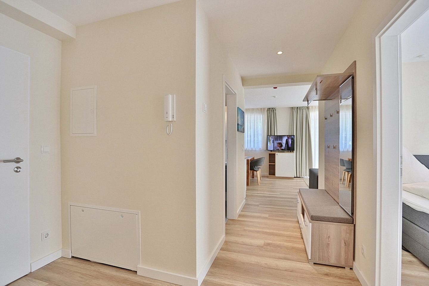A modern apartment with a hallway leading to a living area, a dining space, and a bedroom with a large mirror.