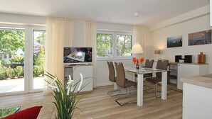 Un soggiorno moderno con un tavolo da pranzo in vetro, posti a sedere confortevoli, una TV a schermo piatto e vista su piante.