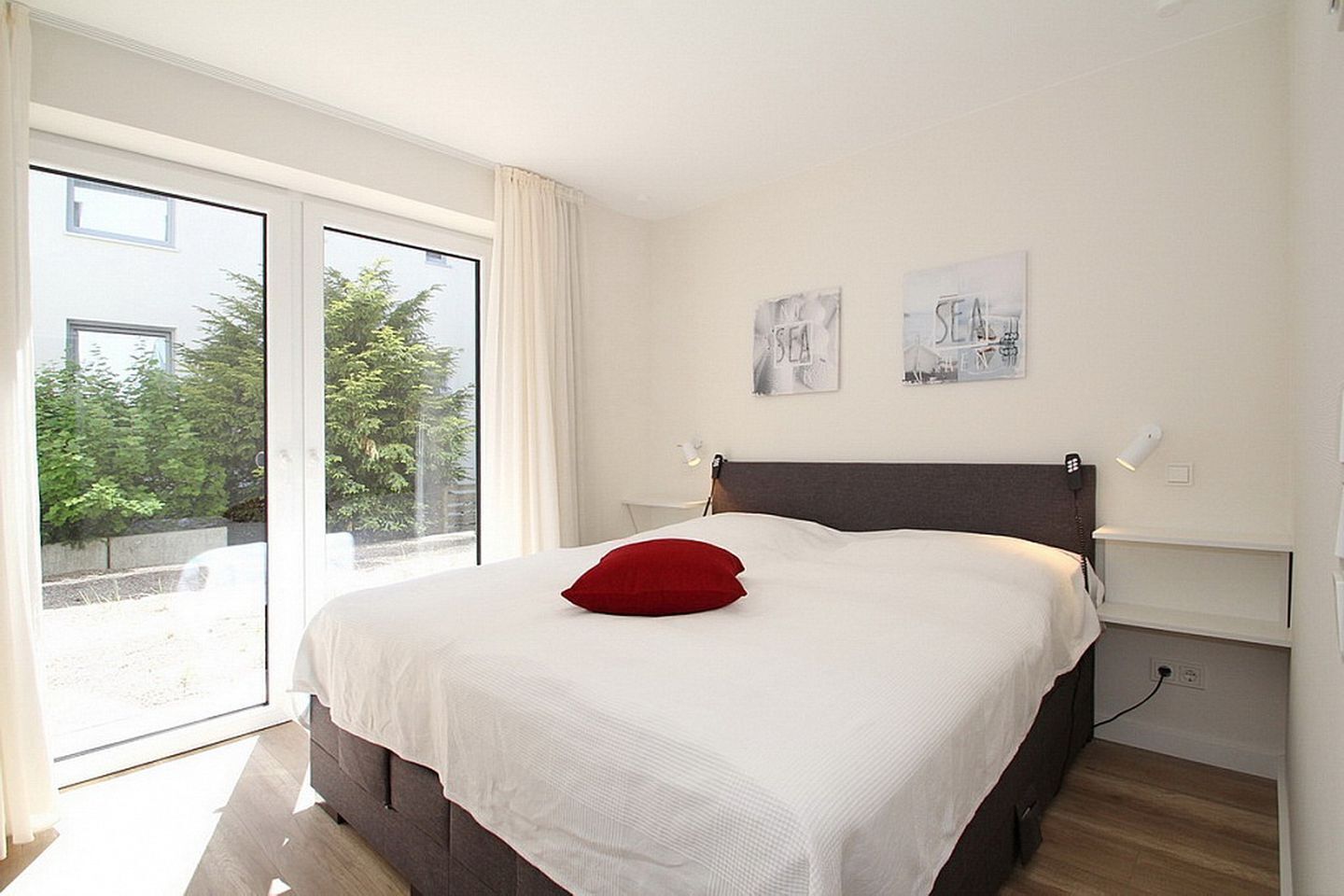 A bedroom with a large bed, a red pillow, and two wall art pieces.