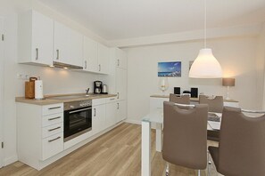 A modern kitchen with white cabinets, a wooden countertop, and a dining area with a glass table and brown chairs. - Villa Stern Apartment 6 - Villa Stern (Timmendorfer Strand)