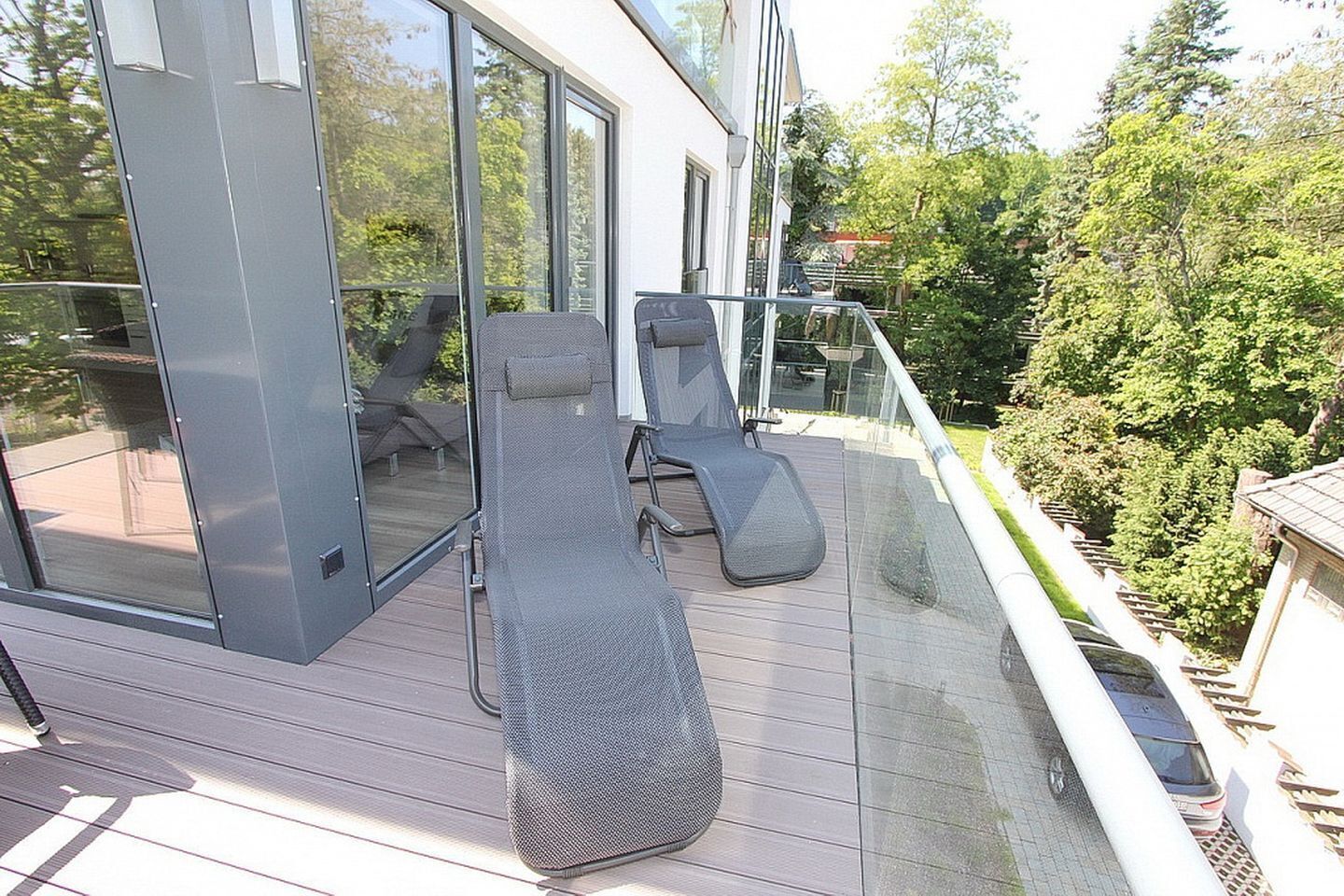 Una terrazza esterna moderna con ringhiere in vetro, due poltrone relax e un'ampia vetrata scorrevole che dà accesso a un ambiente interno.