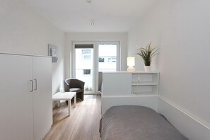 A small, modern room with a bed, a desk, a chair, a plant, and a window. - Villa Stern Apartment 10 - Villa Stern (Timmendorfer Strand)