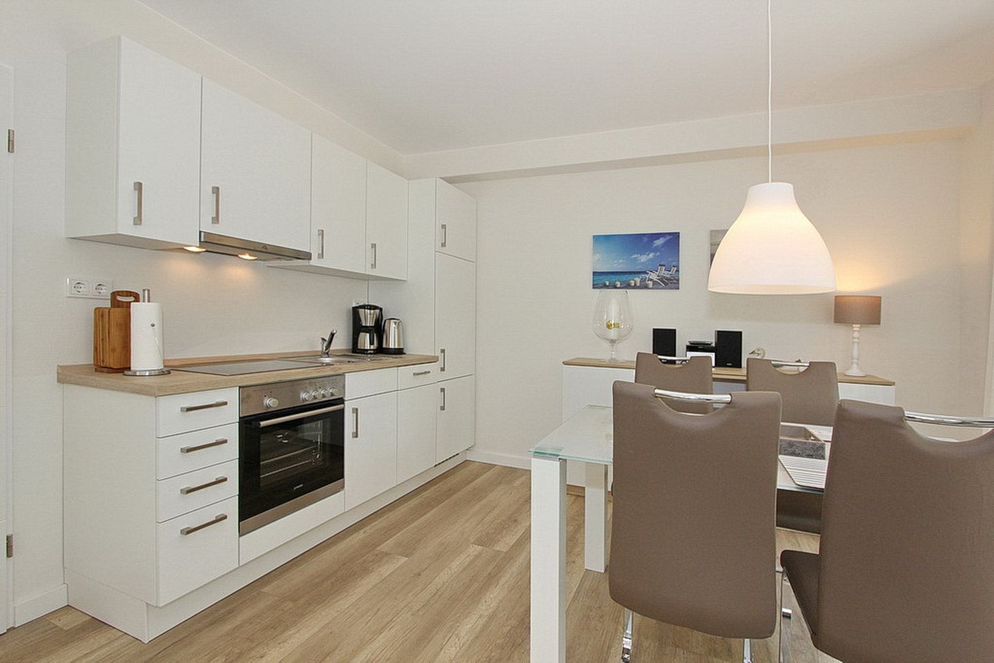 A modern kitchen with white cabinets, a wooden countertop, and a dining area with a glass table and brown chairs.