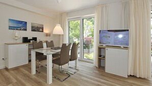 A modern hotel room with a dining area, a television, and a large window with curtains. - Villa Stern Apartment 10 - Villa Stern (Timmendorfer Strand)