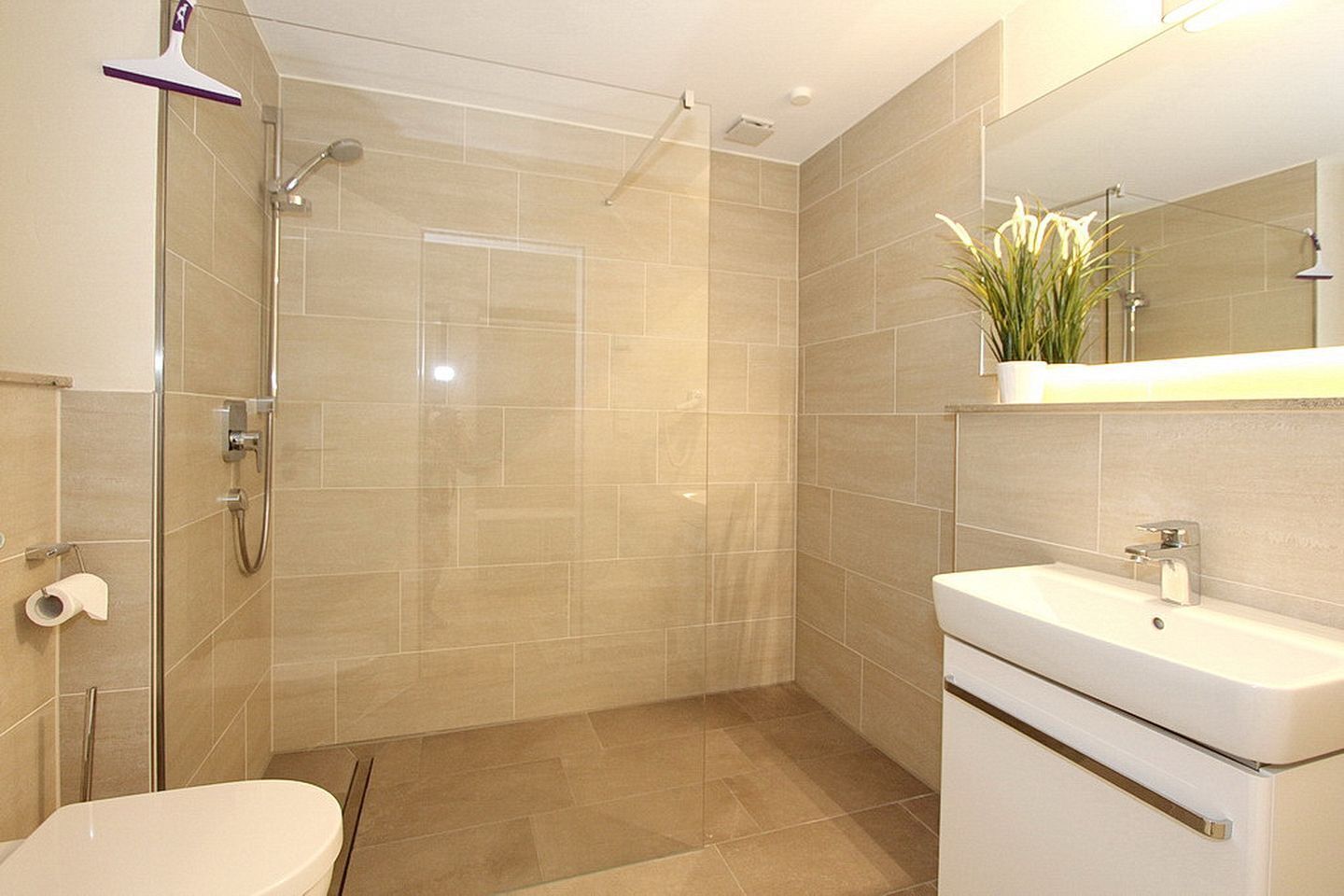 Een moderne badkamer met douche, toilet en wastafel.