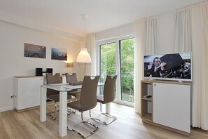 Une chambre d’hôtel moderne dotée d’un coin repas, d’une télévision et d’un balcon offrant une vue sur la verdure.