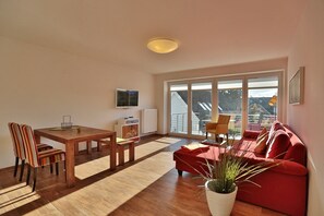 A modern living room with a wooden dining table, chairs, a red sofa, and a large window with a view of the outside.