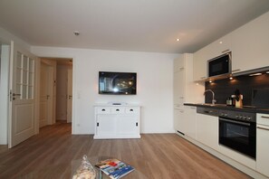 A modern kitchen with white cabinetry, a microwave, an oven, and a flat-screen TV mounted above the cabinets.