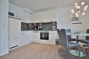 A modern kitchen with white cabinets, a built-in oven, and a dining area with a glass table and metal chairs.