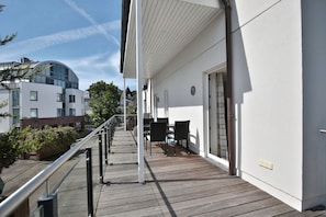 A wooden deck with outdoor seating, a glass balustrade, and a white building with a modern design.