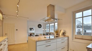 Una cocina moderna con una isla grande, armarios blancos y una campana extractora de acero inoxidable.