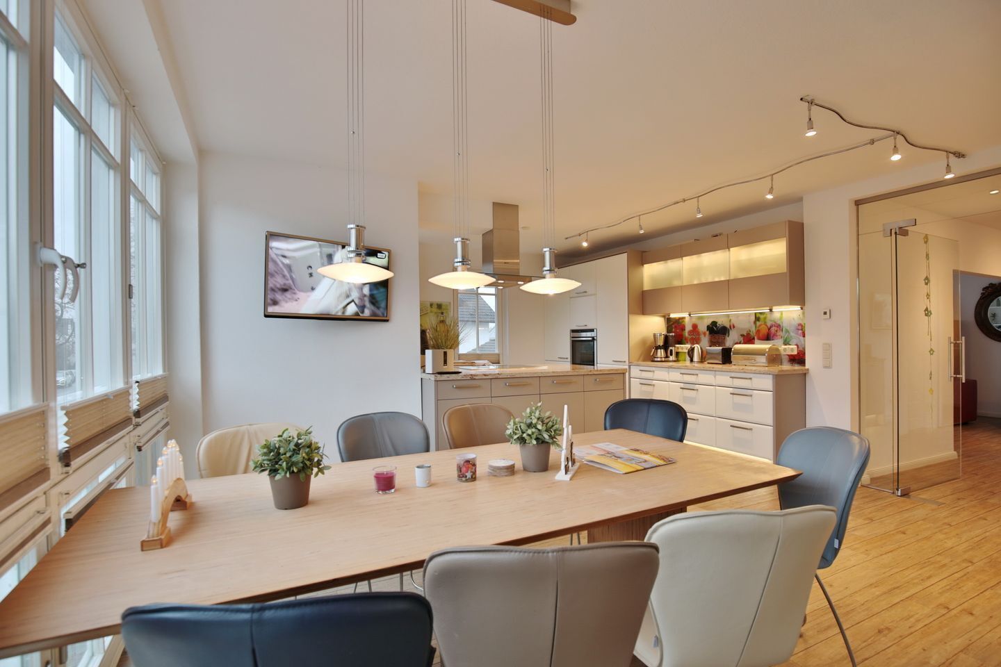 A modern kitchen with pendant lighting, a dining area with a long table, and a view of the adjacent living space.