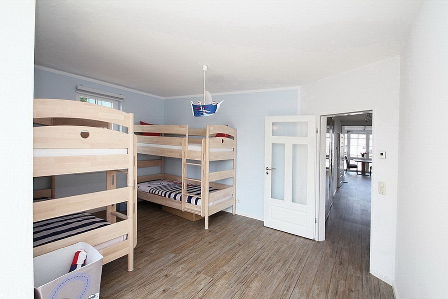 A room with bunk beds, a white door, and a hallway leading to another room.