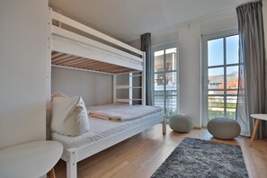Une chambre avec un lit superposé, une fenêtre, une petite table et un tapis.