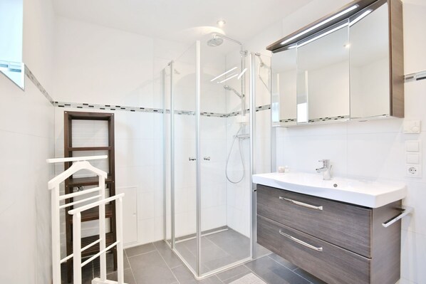 A modern bathroom with a glass shower enclosure, a white sink, and a wooden vanity.