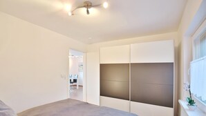 A bedroom with a bed, a wardrobe, and a window with a plant.