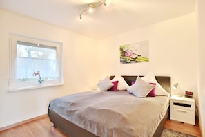 Un dormitorio con cama, mesita de noche, lámpara y ventana con una planta de orquídea.