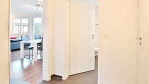 A hallway leading to a dining area with a table and chairs, a sofa, and a view of the outdoors.