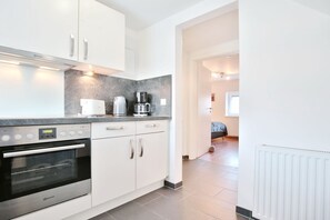 Una cocina moderna con armarios blancos, horno empotrado y cafetera.