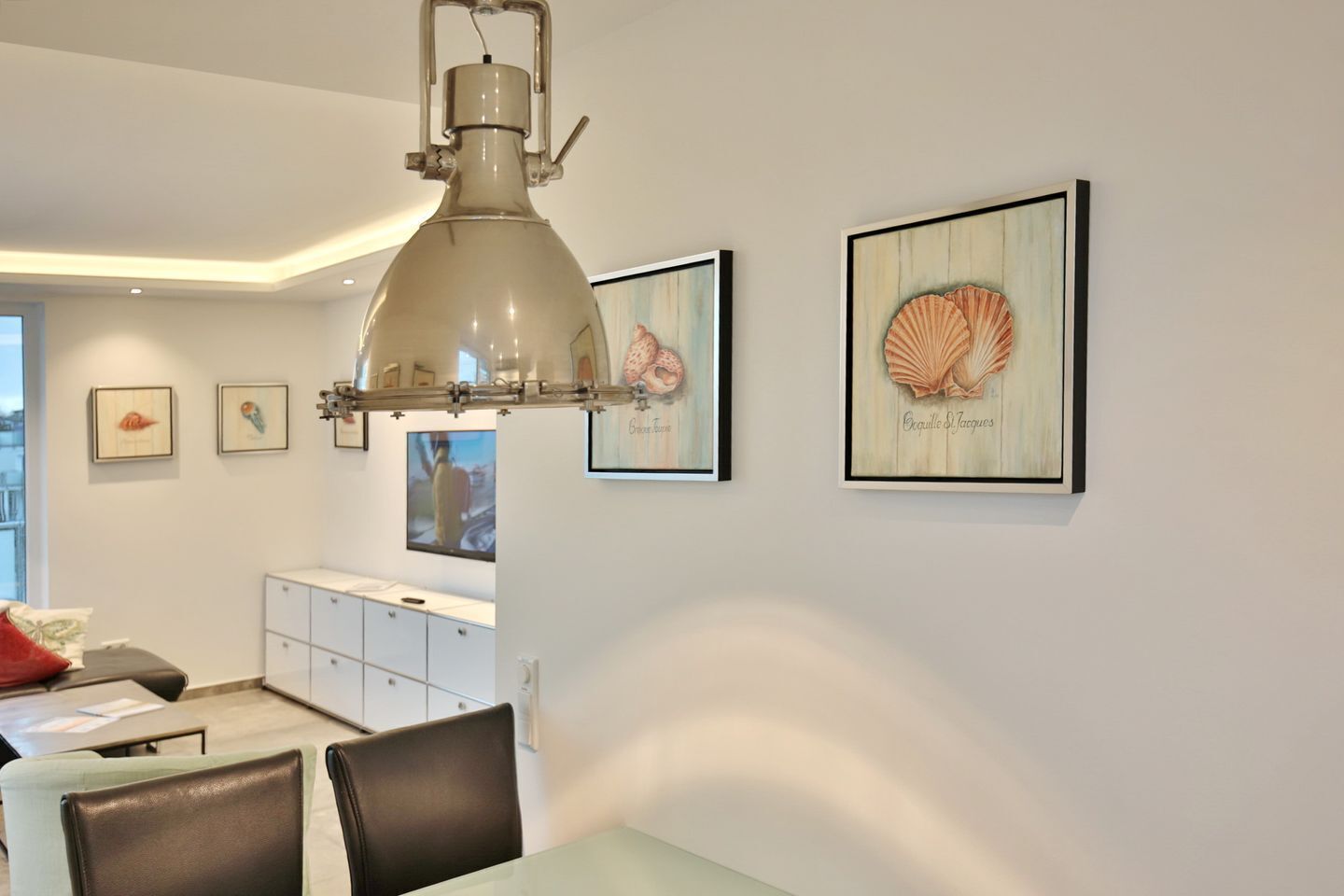 A modern dining area with a pendant light, framed artwork, and a white cabinet.