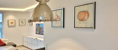 A modern dining area with a pendant light, framed artwork, and a white cabinet.