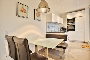 Una cocina moderna con armarios blancos, salpicadero de mármol y una zona de comedor con mesa de vidrio y sillas de cuero.
