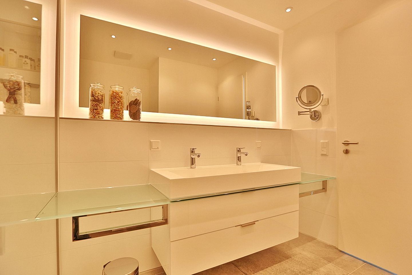 A modern bathroom with a glass vanity, two sinks, and a large mirror.