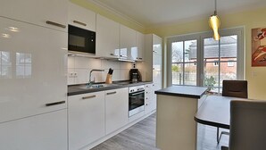 A modern kitchen with white cabinets, a black microwave, and a coffee maker. There is a window with a view of the outside. - Baltic Sea Apartment 1 - Baltic Sea (Timmendorfer Strand)