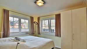 A bedroom with a bed, two windows with curtains, a wardrobe, and a ceiling light fixture. - Baltic Sea Apartment 1 - Baltic Sea (Timmendorfer Strand)