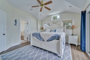 A bedroom with a white bed, a ceiling fan, a nightstand, and a window with blinds.