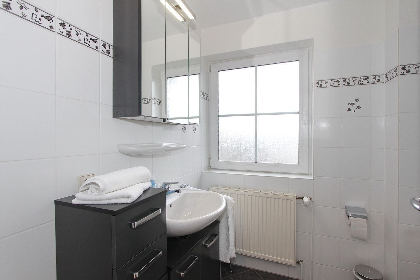 A modern bathroom with a white sink, dark vanity, and a large mirror.