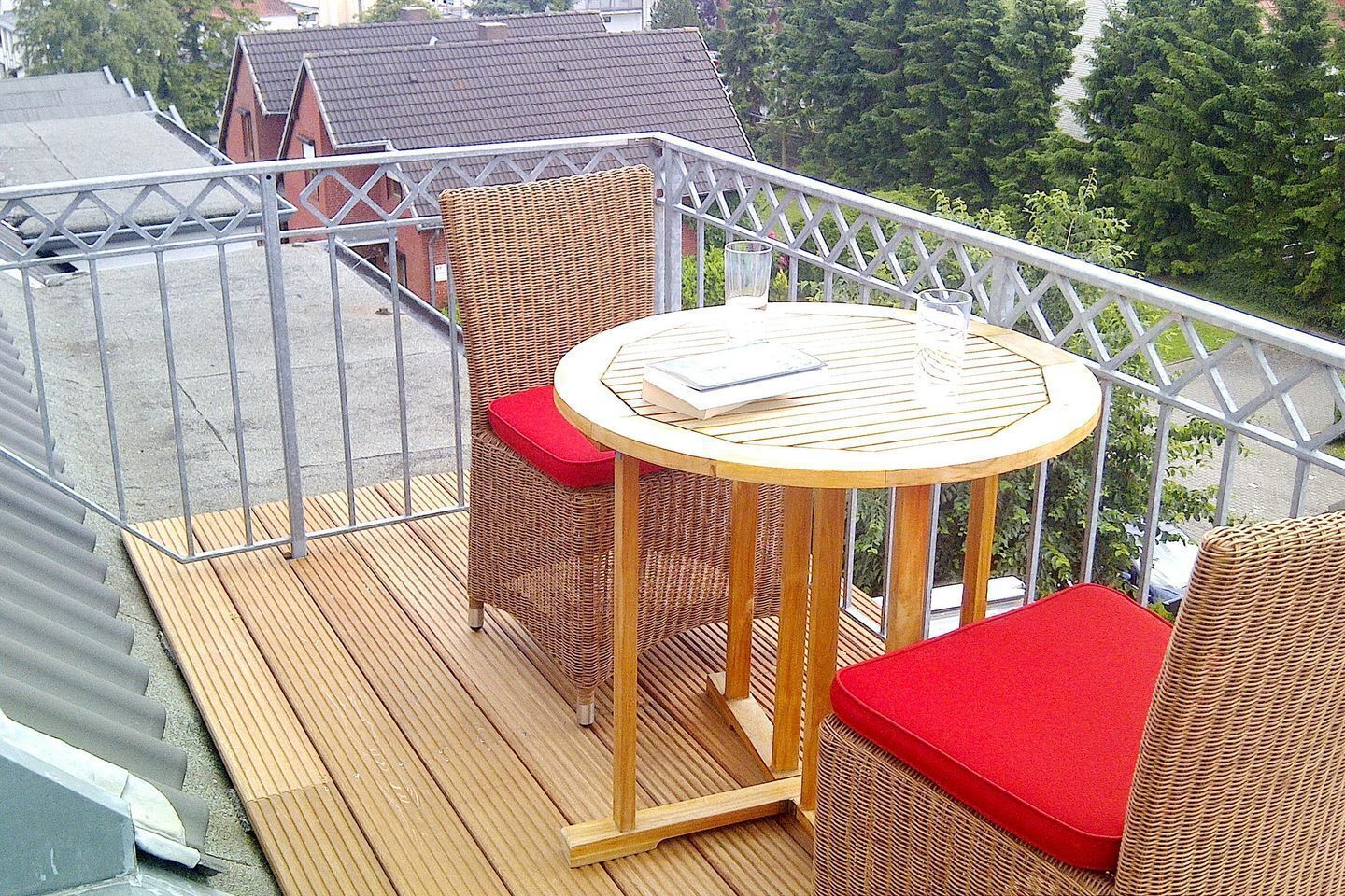 A balcony with wicker furniture, a round table, and red cushions.