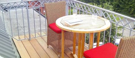 A balcony with wicker furniture, a round table, and red cushions.