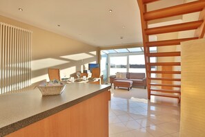 A modern kitchen with a wooden counter, a dining area with a table set for two, and a cozy living space with a sofa and a TV. - Residenz Alte Bergstrasse Apartment 21 - Residenz Alte Bergstrasse (Scharbeutz)