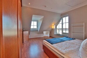 Una camera da letto con soffitto spiovente, un letto, una sedia, una cassettiera e una finestra con vista.