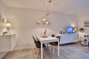 A modern kitchen with white cabinetry, a dining table with chairs, pendant lights, a television, and a small plant. - Residenz Alte Bergstrasse Apartment 4 - Residenz Alte Bergstrasse (Scharbeutz)