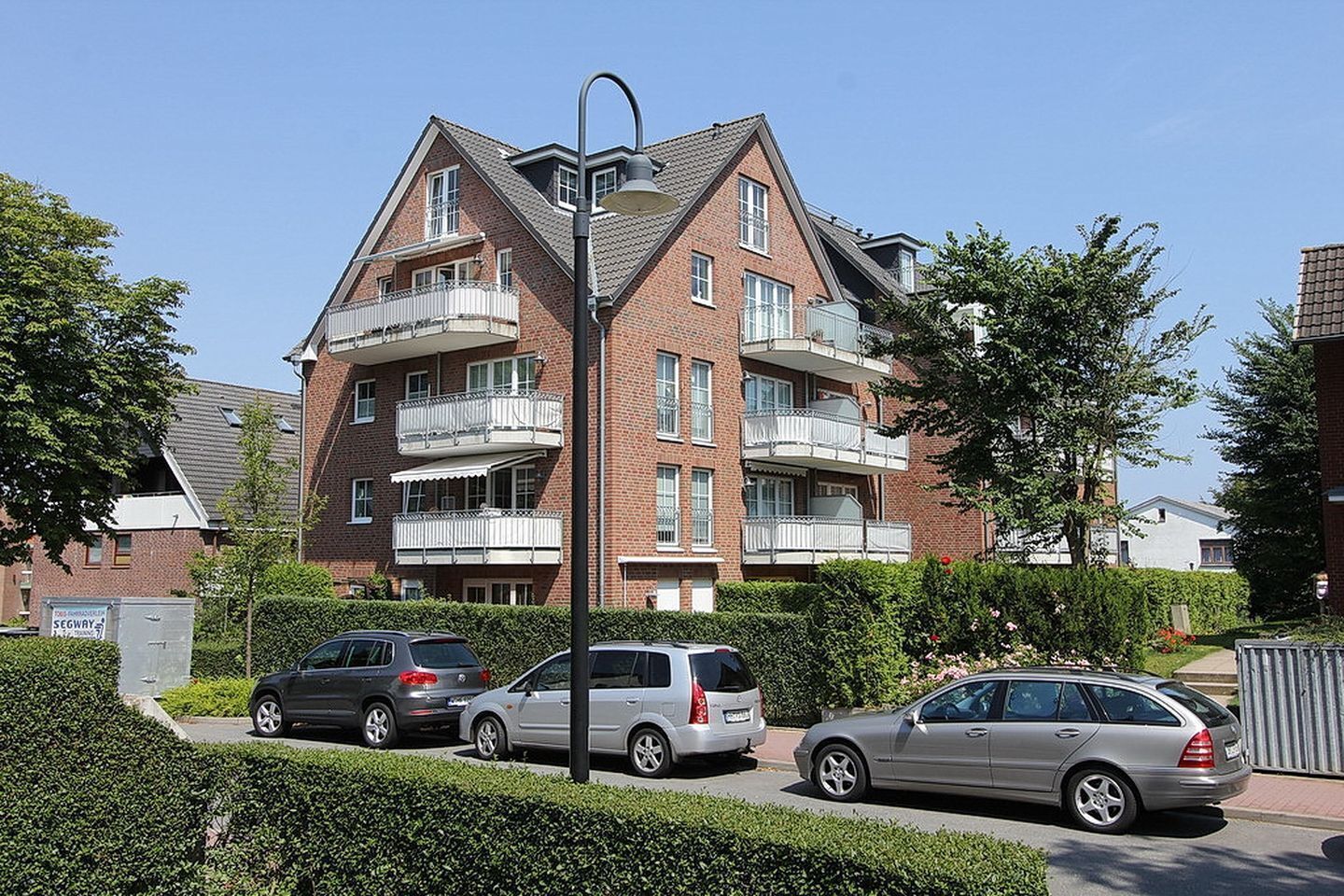 A multi-story residential building with balconies, a paved driveway, and parked cars.