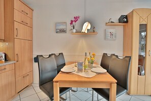 Un coin repas avec une table en bois, deux chaises en cuir noir, une petite étagère avec une lampe et un tableau encadré au mur.