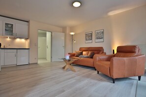 En moderne lejlighed med et køkken, en opholdsstue med sofa og lænestole, samt et spisebord.