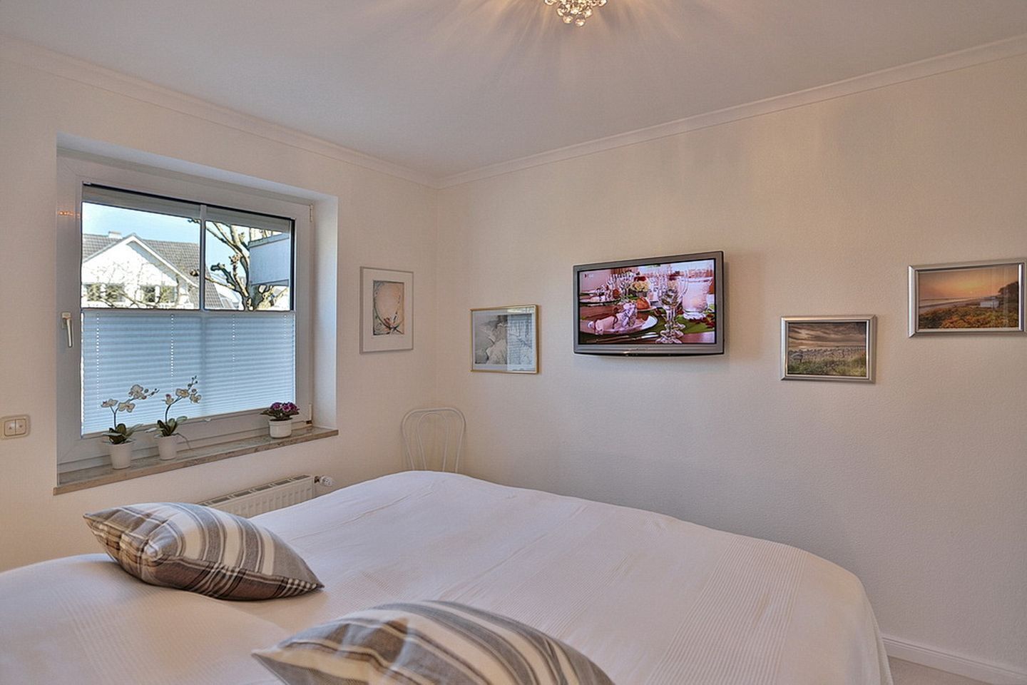 Een slaapkamer met een groot bed, een raam met zonwering en meerdere ingelijste foto's aan de muur.