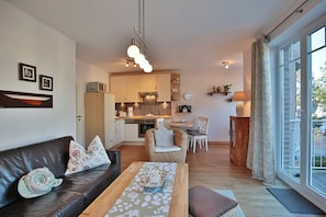 Un espacio habitable compacto con sofá, mesa de comedor, zona de cocina y vistas amplias a través de grandes ventanales.